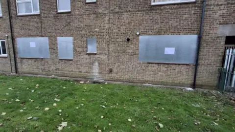 Hull City Council A brick property with its windows closed up by pieces of metal. There is grass with leaves on in front of the property.
