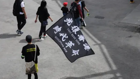 Reagan Yip Several people walking holding a flag which reads 'Free Hong Kong, Revolution Now'