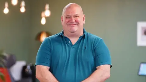 Supplied Image of Mark. He is smiling for the camera and is wearing a blue polo shirt.