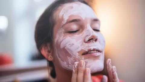 A woman with eyes closed putting cream on her face