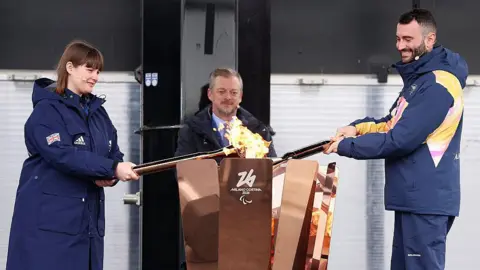 Getty Images Millie Knight of ParalympicsGB and Andrea Macri of Paralympics Italy light the Paralympic Flame cauldron during the Paralympic flame lighting ceremony for the Milano Cortina 2026 Paralympic Winter Games at Stoke Mandeville Stadium 