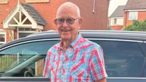A man in a colourful shirt in front of a car