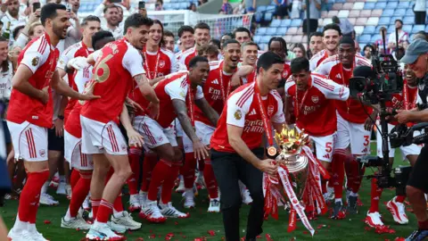 Action Images/Reuters Arsenal manager Mikel Arteta holds the Premier League trophy up in front of the Arsenal team.