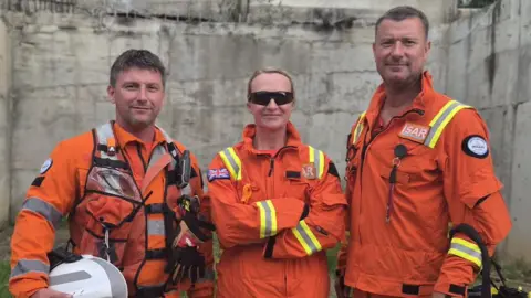 Three firefighters dressed in orange boiler suits.