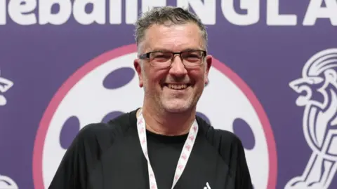 Richard Love, a man who is looking at the camera and smiling. He is wearing a black sports top and has a medal round his neck. 