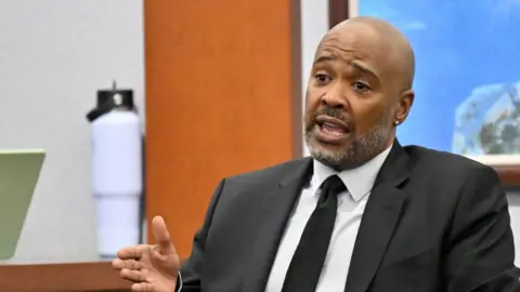 A man in a suit and tie testifies.