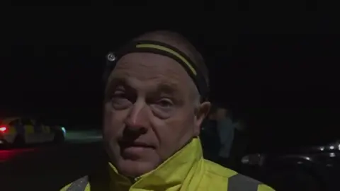 A man in a high vis jacket wearing a head torch 