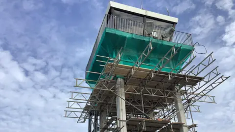 Alderney Airport control tower with scaffolding and netting installed around it.