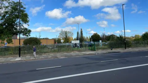 Wide shot of an empty A20 where the crash happened. A man is pictured walking down the path alongside the road in front of a leisure centre