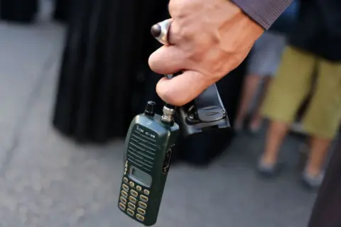 A man holds an Icom walkie talkie device after he removed the battery during the funeral of persons killed when hundreds of paging devices exploded in a deadly wave across Lebanon the previous day, in Beirut's southern suburbs on September 18