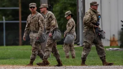 Four national guard troops from Texas are wearing camouflage uniforms and walking on grass