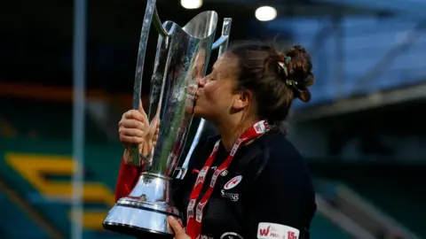 Getty Images Georgina Gulliver kissing a large silver trophy with a medal round her neck. 