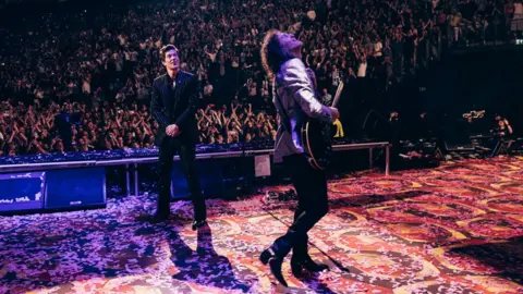 Chris Phelps Brandon Flowers e Dave Keuning no palco olhando para a tela