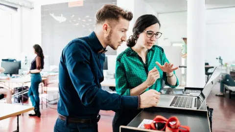 A man and a woman in an office looking at a laptop computer