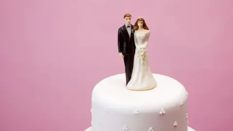 Picture of two figurines - a bride and a groom - sitting on top of a wedding cake