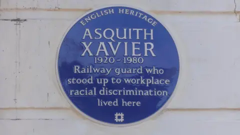 English Heritage A round blue plaque bearing the name and dates of Asquith Xavier 