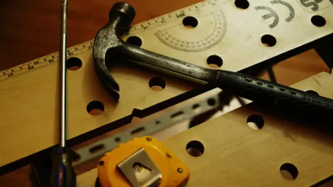 A hammer, chisel and tape measure lie on some planks of wood.
