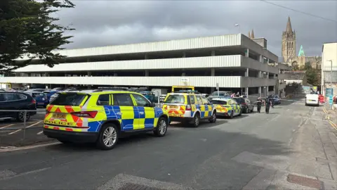 Three police cars parked outside a concrete multi-storey car park