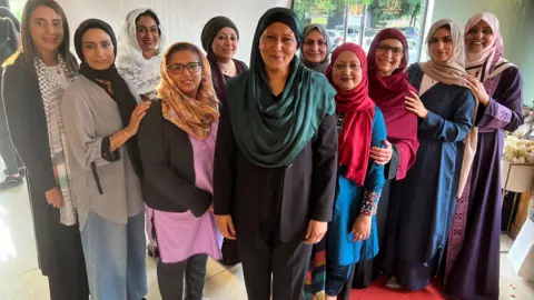 A group of 11 women, the majority are visibly Muslim as they wear headscarves and long robes.
