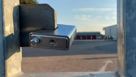 A padlock on a gate with a test centre in a soft focus in the background