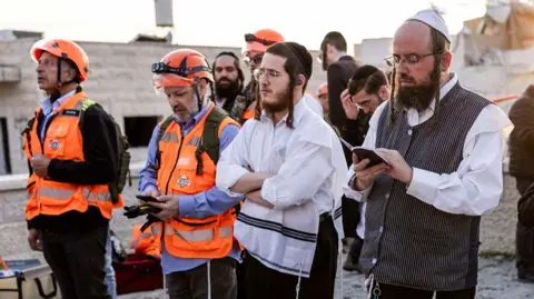 Jewish men pray at the scene of a missile attack in Bet Shemesh, some 30 kilometres west of Jerusalem