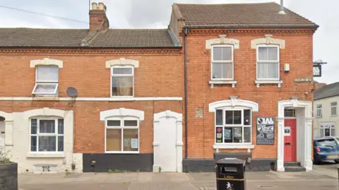 Google A red brick terraced building. A black sign with "Lab" written on it is next to a red door. 