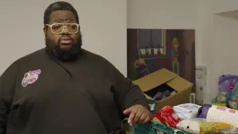 Solomon Smith leans one arm on a green crate of donated food.