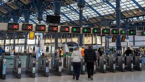 Two people walking through barriers at Brighton Railway Station.