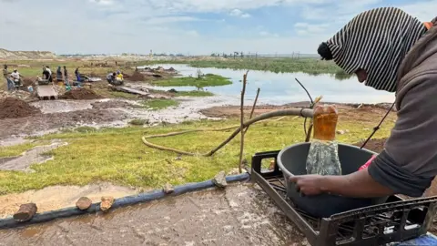 Thuthuka Zondi/BBC A man wearing a white and black stripped balaclava washes soil searching for gold.