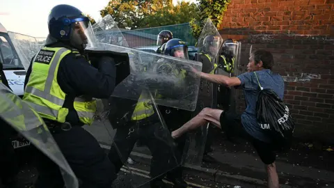 Getty Images Police with riot shields confront a man kicking them
