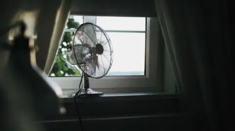 Getty Images A silver fan is sitting on a bedroom windowsill. 