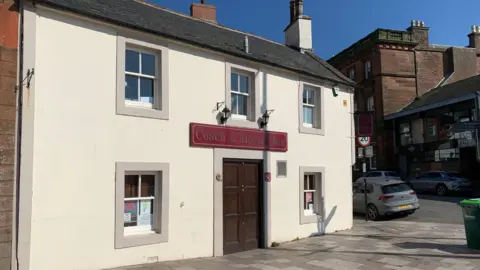 The cream coloured facade of the Coach and Horses pub in Dumfries with a purple sign carrying its name on a rare sunny day