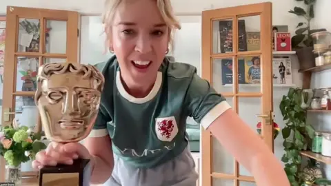 Lauren Evans wearing a green Welsh football shirt holding a golden BAFTA statue