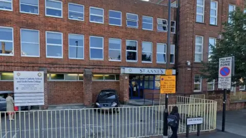 Google A boxy red bricked building on a main road. A 'St Anne's' sign overhangs a doorway entrance, while a larger school sign stands in the school car park.