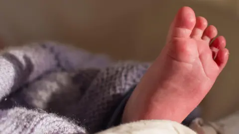A baby's foot emerges from under a light blue and grey blanket