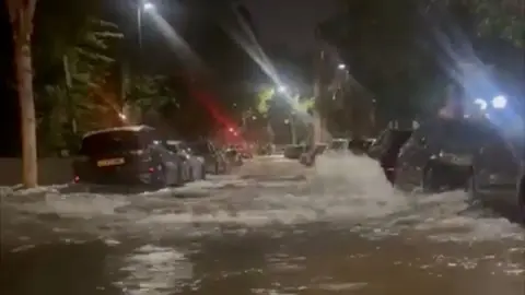 A road lined with cars on both sides, at night, with water flowing down the middle