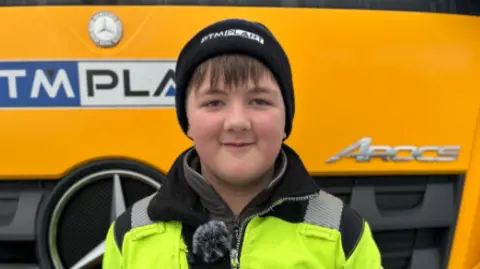 Jamie Monaghan, a teenage boy, is wearing a black woolly hat and a yellow high-vis jacket