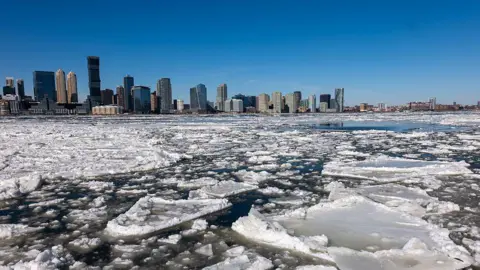 Ice floes are seen covering part of the Hudson River as skyscrapers are seen in the background along the Manhattan shoreline 