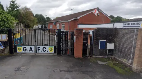 The outside of Gornal Athletic football club, showing black gates leading to a car park