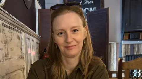 Hannah Tabram Hannah Tabram is sitting at a restaurant/pub table. She is wearing a greenish-brown shirt and looking directly at the camera.