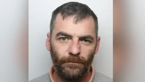 West Yorkshire Police Matthew Harrison's police custody image. He is a white man with a brown, greying beard. He has short dark hair.