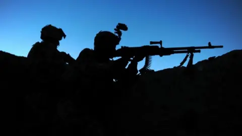 Two soldiers seen in silhouette against a blue sky