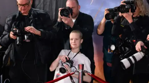 Teenage photographer Liz Hatton on the red carpet surrounded by older, male photographers 