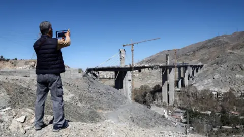 A man uses his phone to photograph the remains of the B1 bridge following a US air strike, in Karaj, northern Iran (3 April 2026)