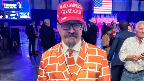 Blake Marnell wears his brick patterned suit and a red Maga hat