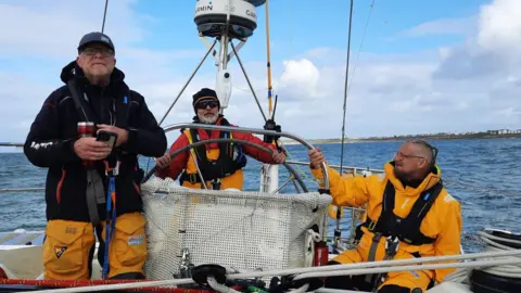 Clipper Ventures Bob Brown steering a yacht accompanied by two other crew members
