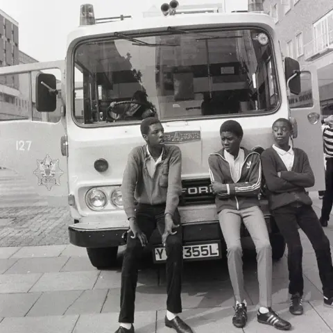Alan Van Wijgerden Three boys lean against a 1950s Ford West Midlands fire engine