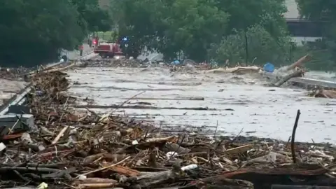 Debris is pictured at the side of a large pool of floodwater with trees and a fire engine seen in the background, in a grab from footage following flooding along the Guadalupe River in Kerr County, Texas on 4 July.