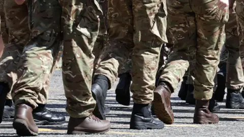 Soldiers' legs in uniform and boots walking from right to left.