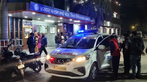 Pradeep Kashyap/BBC A group of men stand near a white ambulance car parked outside the entrance of the district hospital building in Madhya Pradesh's Satna